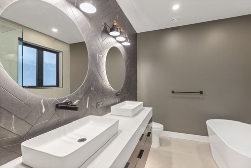 Modern bathroom with illuminated mirrors, double vanity, and freestanding tub